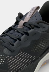 Chaussure de course noire avec un dessus texturé, des détails en mesh et des accents réfléchissants. Semelle épaisse avec un léger amorti, conçue pour la performance.