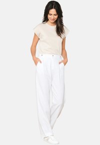 Beige short-sleeve top with a relaxed fit, paired with white wide-leg trousers featuring side pockets and gold buttons. White sneakers.