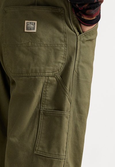 Pantaloni cargo color khaki con una tasca rinforzata, dettagli cuciti e un'etichetta in tessuto con la dicitura "Polo RL Quality Garments" sul retro.