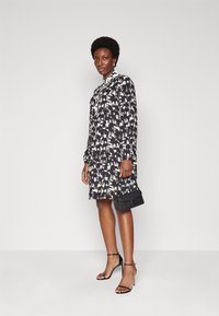 Black and white long-sleeve dress with animal print patterns, features a collar, mid-thigh length, paired with a black handbag and strappy heels.