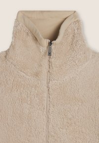 Giacca in pile beige con colletto alto, dotata di zip frontale completa e dettagli a coste sul collo, texture morbida e senza motivi visibili.