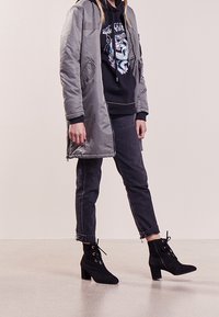Abrigo acolchado gris con capucha, sudadera gráfica negra debajo, jeans oscuros y botas negras hasta el tobillo con detalle de cordones y tacones cuadrados.