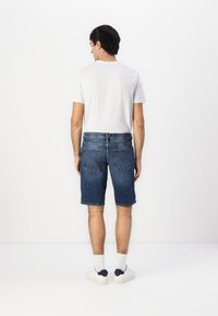 Shorts en denim bleu foncé avec un ourlet effiloché, deux poches arrière et une taille standard, associés à un T-shirt blanc uni et des baskets.