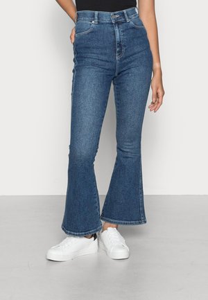 Jean flare taille haute en denim bleu foncé, avec un design classique à cinq poches et une fermeture à l'avant avec un bouton en métal.