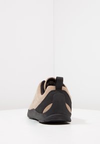 Brown suede shoes with a black textured panel, rounded shape, rear pull tab, and a flexible black rubber sole. Suitable for casual wear.