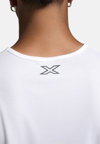 Biała koszulka sportowa z teksturowanej tkaniny, zaokrąglonym dekoltem i czarnym logo "X" umieszczonym w centrum z tyłu.