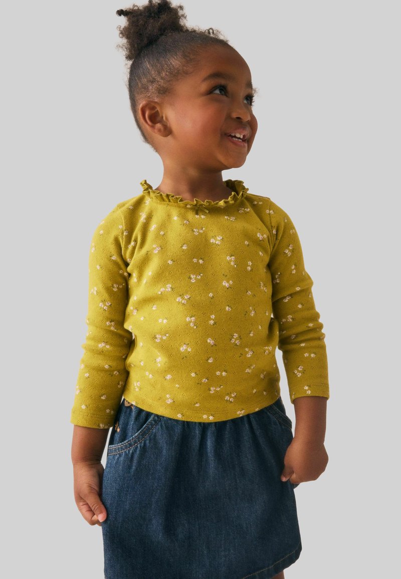 Camicia gialla a maniche lunghe con motivo floreale piccolo e collo arricciato, abbinata a una gonna di denim con vita arricciata e tasca laterale.
