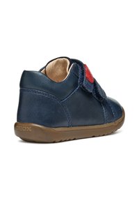 Zapato de cuero azul marino con una correa de velcro, punta redonda y suela de goma marrón. Presenta la marca Geox en el lateral. Textura suave.