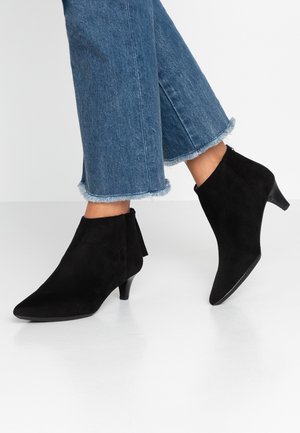 Botas de ante negras hasta el tobillo con puntera afilada y tacón bajo, que cuentan con un zipper lateral y un sutil detalle de borlas en la parte posterior.