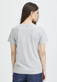 T-shirt gris à manches courtes en tissu doux, avec un col rond et un design minimaliste. Étiquette visible à l'arrière du col.