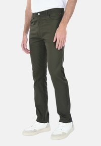 Pantaloni di cotone verde oliva con una vestibilità slim, tasche frontali, passanti per cintura e zip, abbinati a sneakers bianche e grigie.