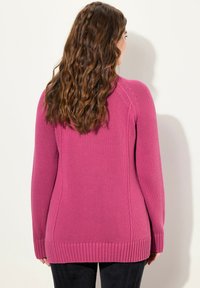 Maglione a maglia magenta con orlo e polsini a coste, con una finitura texturizzata e una forma aderente. Le spaccature laterali aggiungono un dettaglio sottile.