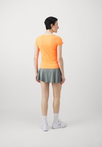 Orange fitted short-sleeve shirt with a round neck, paired with a gray pleated skirt. White athletic socks and light sneakers complete the outfit.