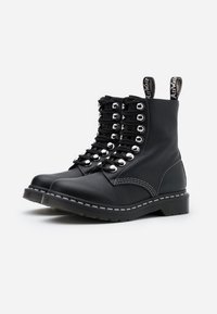 Botas de cuero negro con punta redonda, ojales plateados y cordones negros. Presentan costuras blancas y tiradores en la parte superior para facilitar su uso.