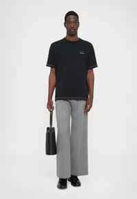 Tricou din bumbac negru cu mâneci scurte și un grafic mic, asortat cu pantaloni evazați gri deschis și purtând o poșetă cilindrică neagră.