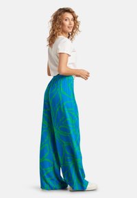 Wijde broek van levendig blauwe stof met een gedurfd groen abstract patroon. Elastische tailleband en lichtgewicht materiaal voor comfort.