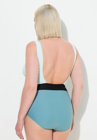 Maillot de bain taille haute avec un design sans dos. Partie supérieure texturée bleu clair avec une ceinture noire, en contraste avec le bas teal uni.