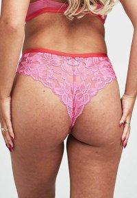Roze kanten string met bloemenpatronen, semi-doorzichtige mesh delen en een contrasterende effen tailleband. De achterkant benadrukt het ontwerp.