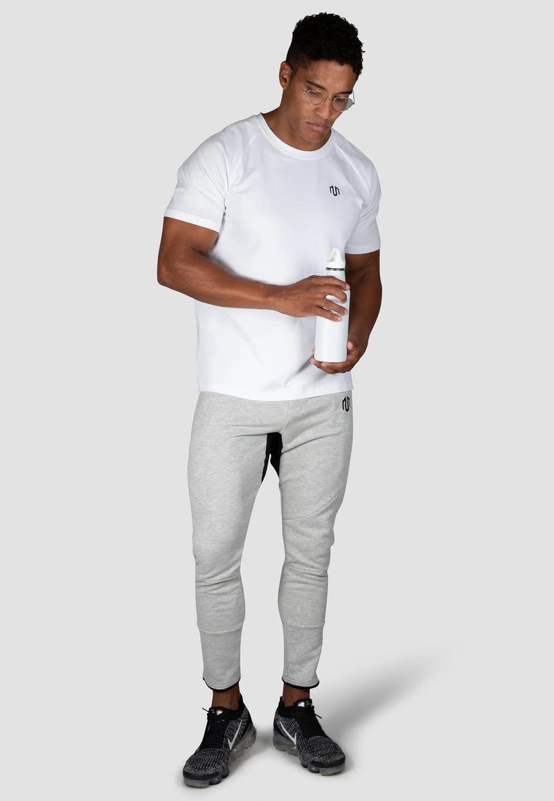 Hvid t-shirt med korte ærmer og et lille logo, grå sweatpants og sorte sportssko. Holder en hvid vandflaske. Enkel, funktionel design.