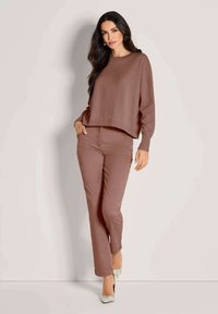 Brauner gestrickter Pullover mit einem cropped Design, kombiniert mit passenden braunen geraden Hosen. Das Model trägt gemusterte High Heels.