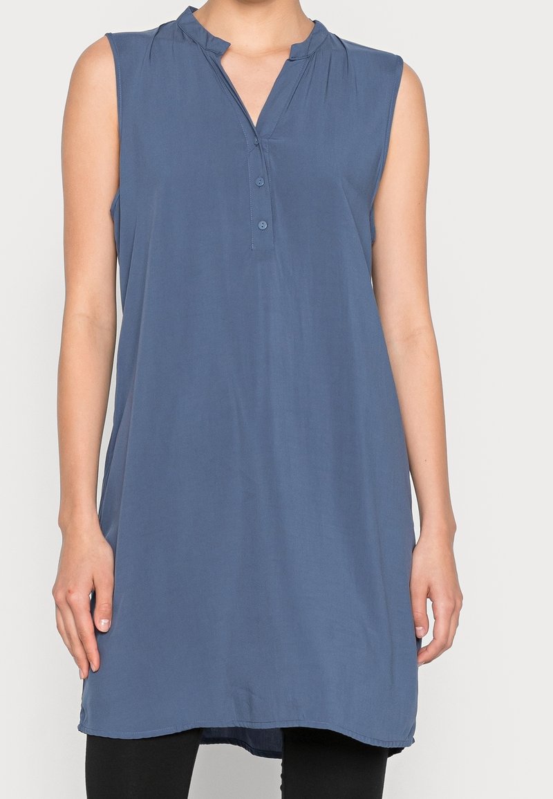 Ärmlose tunika i blått med V-ringning, knappstängning och veckade detaljer, tillverkad av mjukt och lätt material.