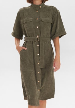 Robe en velours côtelé kaki avec manches courtes, deux poches poitrine et taille ceinturée. Comprend des boutons dorés et une finition texturée.