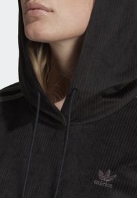 Svart ribbad huvtröja med snören, med en liten mörk logotyp på bröstet och ett strukturerat tygmönster.