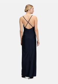 Lång marinblå klänning med en figurnära siluett, spaghettiband och korsad ryggdesign. Slätt tyg och en diskret dragkedjedetalj på baksidan.