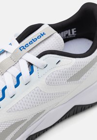 Reebok tenisice s mrežastim gornjim dijelom u bijeloj boji, plavim akcentima i crnim obodom. Teksturirana gumena potplata s oblikovanim dizajnom za potporu.