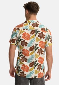 Hombre de espaldas que lleva una camisa de botones de manga corta con un gran estampado floral en naranja, marrón, azul, verde y amarillo sobre fondo blanco.