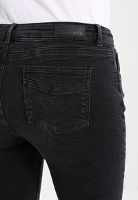 Czarne dżinsy denimowe o teksturowanym wykończeniu, z tylną kieszenią oraz oznaczeniem z czarnej skóry na pasku.}}