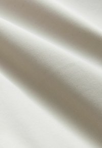 Gros plan d'un tissu lisse beige clair avec une texture fine côtelée et des plis doux créant des ombres douces.