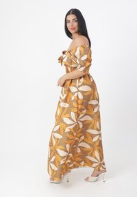 Abito lungo in beige caldo con grandi motivi floreali gialli e bianchi. Design spalline scoperte, vita elasticizzata, tessuto fluido.