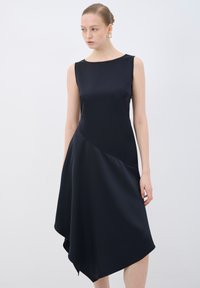 Robe sans manches bleu marine foncé avec un ourlet asymétrique, en satin lisse, décolleté rond et détails en coutures diagonales subtiles.