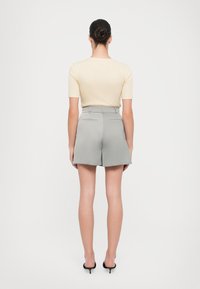 Haut beige clair à manches courtes associé à un short gris taille haute et bien ajusté. Le short est doté de poches arrière et d'une finition lisse et structurée.