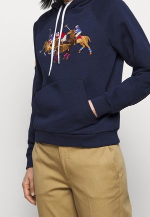 Marineblauwe hoodie met een voorzak en witte trekkoorden, met geborduurde polo spelers te paard in rood, blauw en beige kleuren.