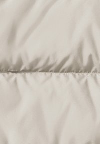 Licht beige behaalde stof met een gladde, glanzende textuur en subtiele plooien, met een horizontale naad in het midden.