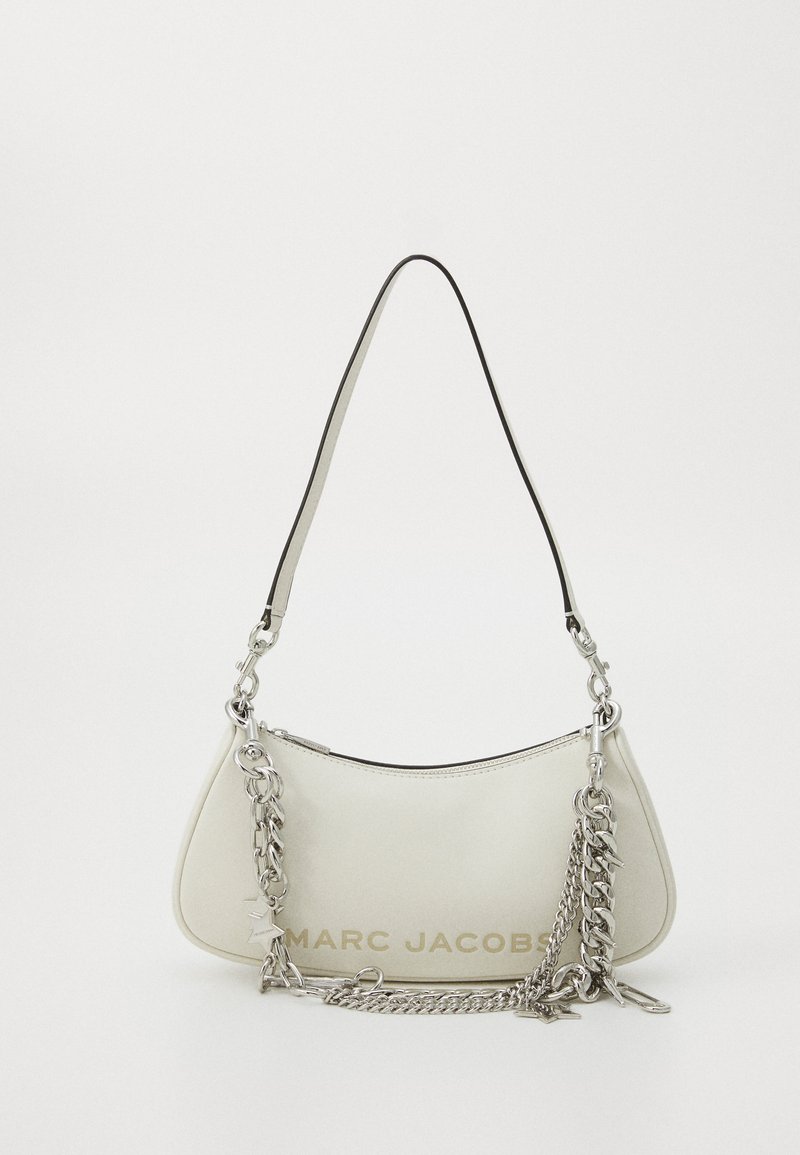 Balta ādas rokassoma ar izliektu formu, kurai ir melna apdare, sudraba ķēdes akcenti un "MARC JACOBS" izspiests zeltā.