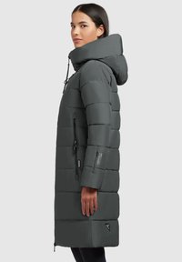 Manteau long matelassé gris foncé avec capuche, doté d'une fermeture éclair à l'avant, de poches latérales et de coutures horizontales. Texture lisse et résistante à l'eau.