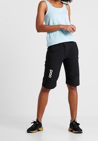 Černé sportovní šortky s volným střihem, s bočními kapsami a bílým logem "POC". Kombinovány s světle modrým tílkem.