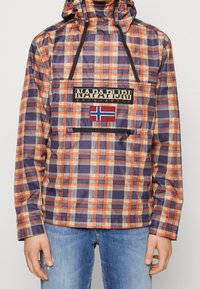 Rød, lilla og cremeternet jakke med lynlåslomme foran, hætte og Napapijri-logo over et norsk flag-patch.