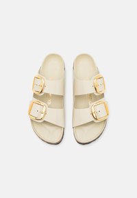 Beige sandalen met twee brede banden, voorzien van gouden gespen, een gladde glanzende afwerking en een lichtbruine contourzool.