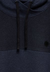 Námořnický modrý mikina s kapucí s texturovanou horní částí, černými šňůrkami a malým logem. Měkká tkanina s hladkým povrchem.