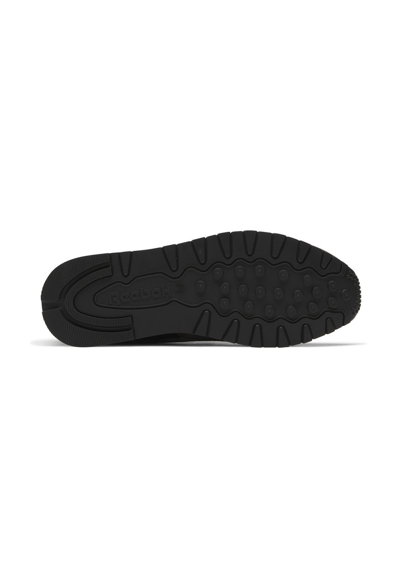 Semelle de chaussure de sport noire en caoutchouc texturé, dotée de motifs circulaires et du logo Reebok, conçue pour l'adhérence et la durabilité.