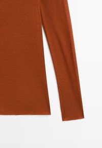 Long-sleeve top in rust orange knit fabric. Features a straight cut with a side slit for ease of movement. Smooth, slightly textured surface.