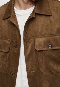 Veste en daim marron avec un col pointu, des poches poitrine et des fermetures à boutons. Caractérisée par une texture douce et une coupe décontractée.