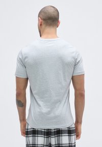 Grå t-shirt med korte ærmer, bomuldsblanding, tætsiddende design, glat tekstur, båret med sort-hvide ternede bukser, set bagfra.