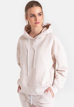 Jasno beżowa bluza z kapturem z miękkiego materiału, z przednią kieszenią, sznurkiem w kapturze i ściągaczami przy rękawach. Prosty design z minimalnymi detalami.