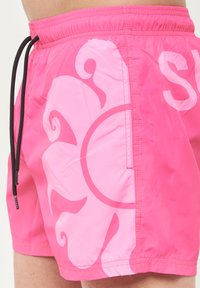 Pantaloncini da bagno rosa con un ampio motivo a vortice di un rosa chiaro, vita elastica con cordino nero e dettagli sulle cuciture laterali.