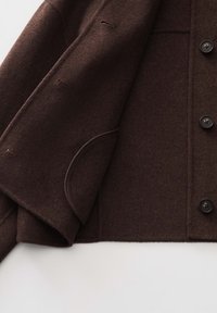 Donkerbruine wollen jas met knopen aan de voorkant, drie zichtbare knopen, knoopsgaten en een afgerond klepzakdetail op een witte achtergrond.